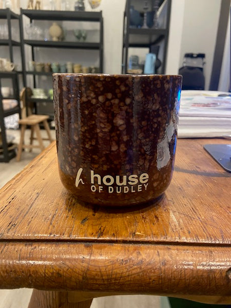 Ceramic mug with 'House of Dudley' branding on a wooden surface.