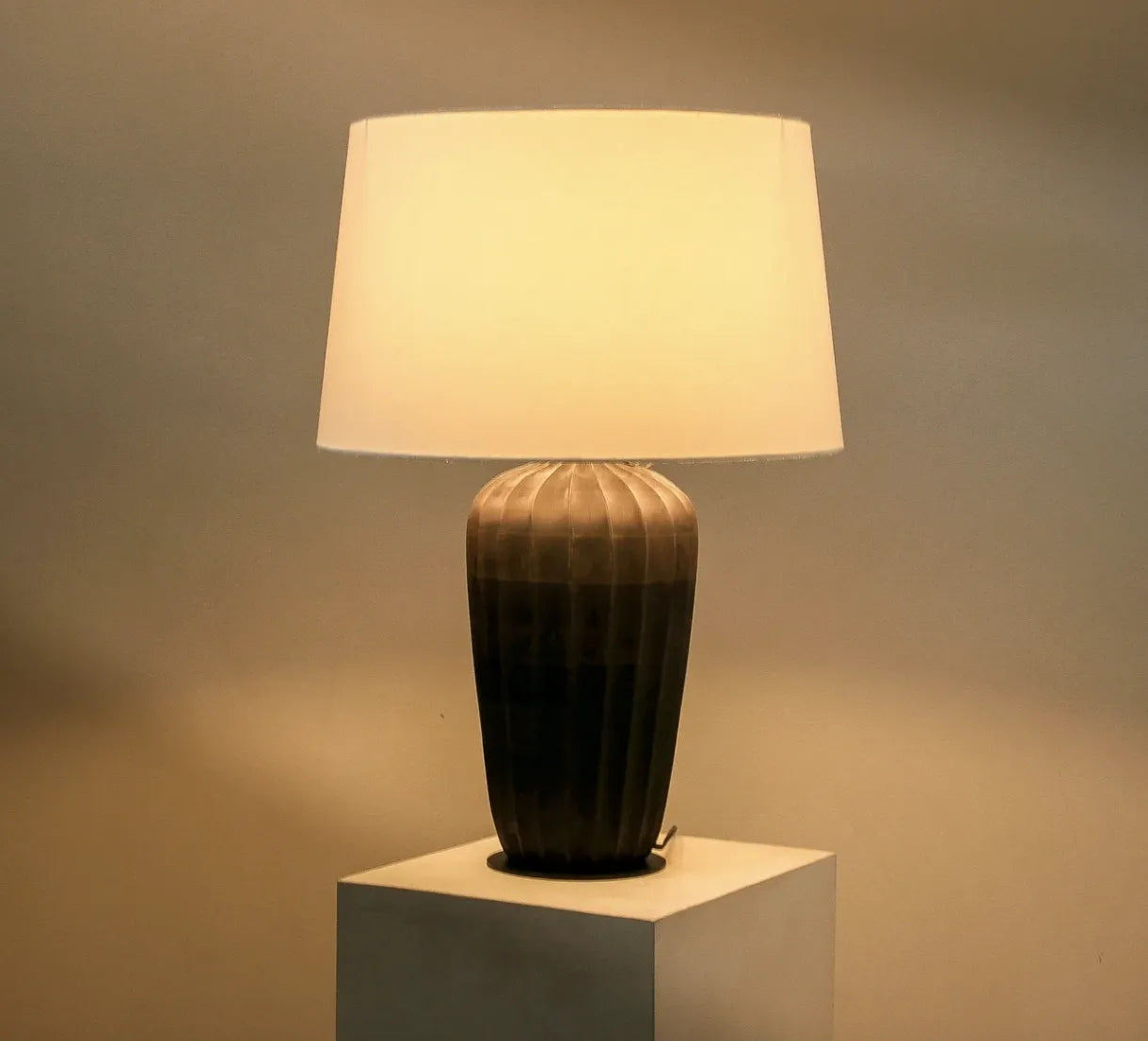 Kai table lamp lit at night casting warm ambient light from its cotton shade
