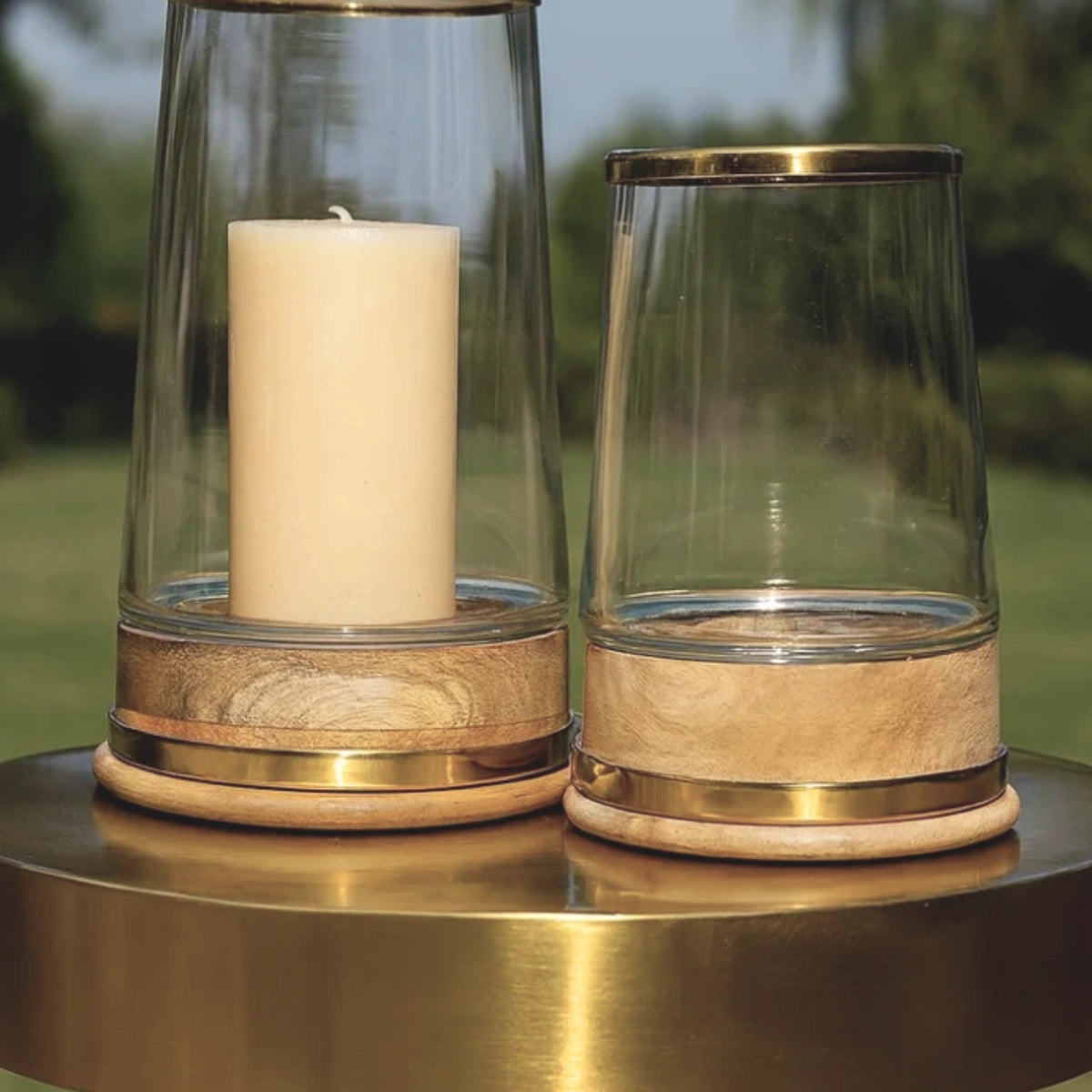Glass hurricane candle holders with brass bands and turned wood bases, small and large shown together