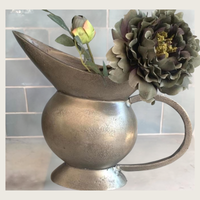 Thumbnail for Decorative metal pitcher with flowers against a tiled wall background